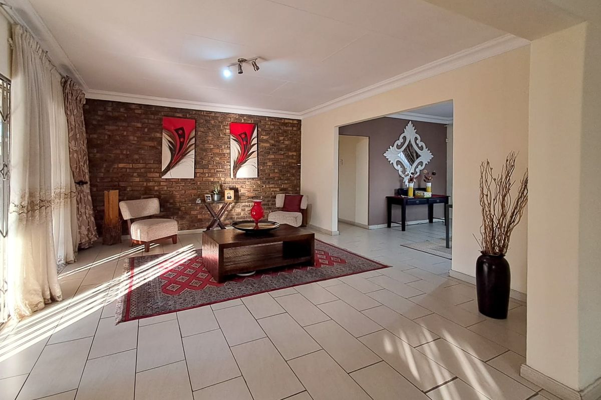 Spacious living room featuring an exposed brick accent wall, neutral ceramic floor tiles, and coved ceiling detailing with recessed lighting.