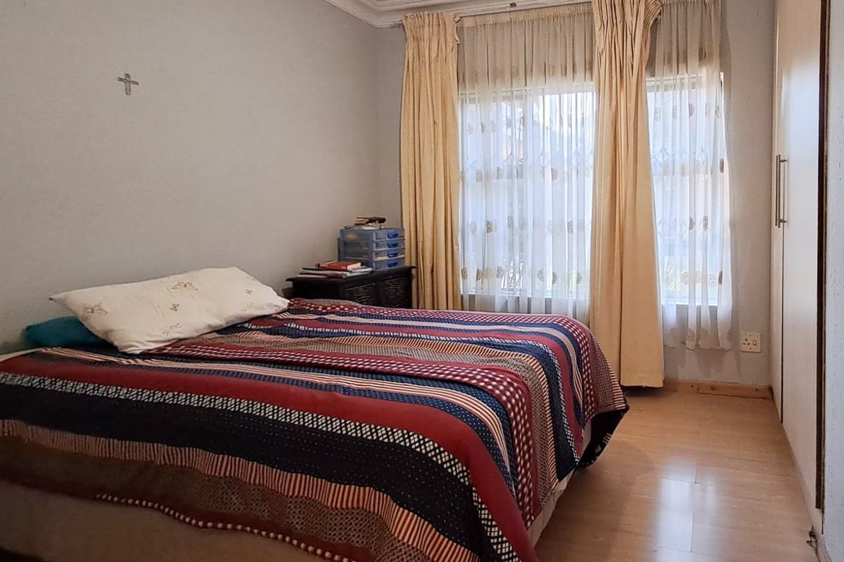 A functional bedroom featuring laminate flooring, a built-in wardrobe, and natural light through window curtains.