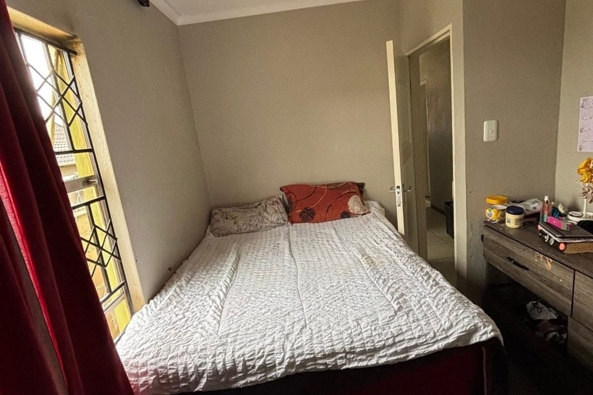 A standard bedroom featuring tiled flooring, coving, and security bars on the window, providing a functional living space.