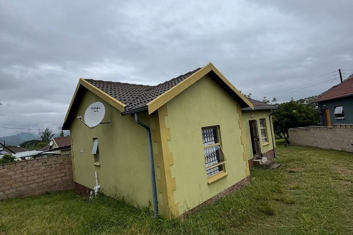 Rear view of a detached house featuring a tiled roof, security bars on windows, and a surrounding brick boundary wall on a grassed plot.