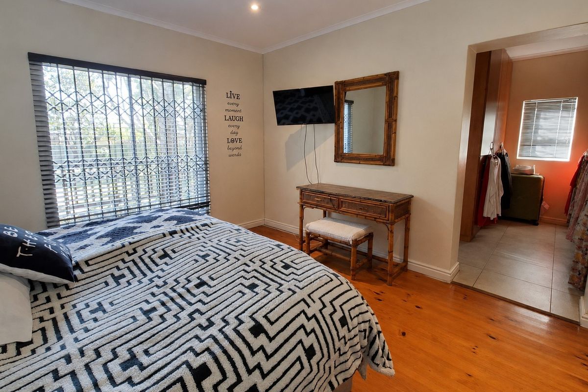 A well-maintained bedroom featuring warm timber flooring, recessed lighting, and an adjoining walk-in closet area with a security gate on the window.