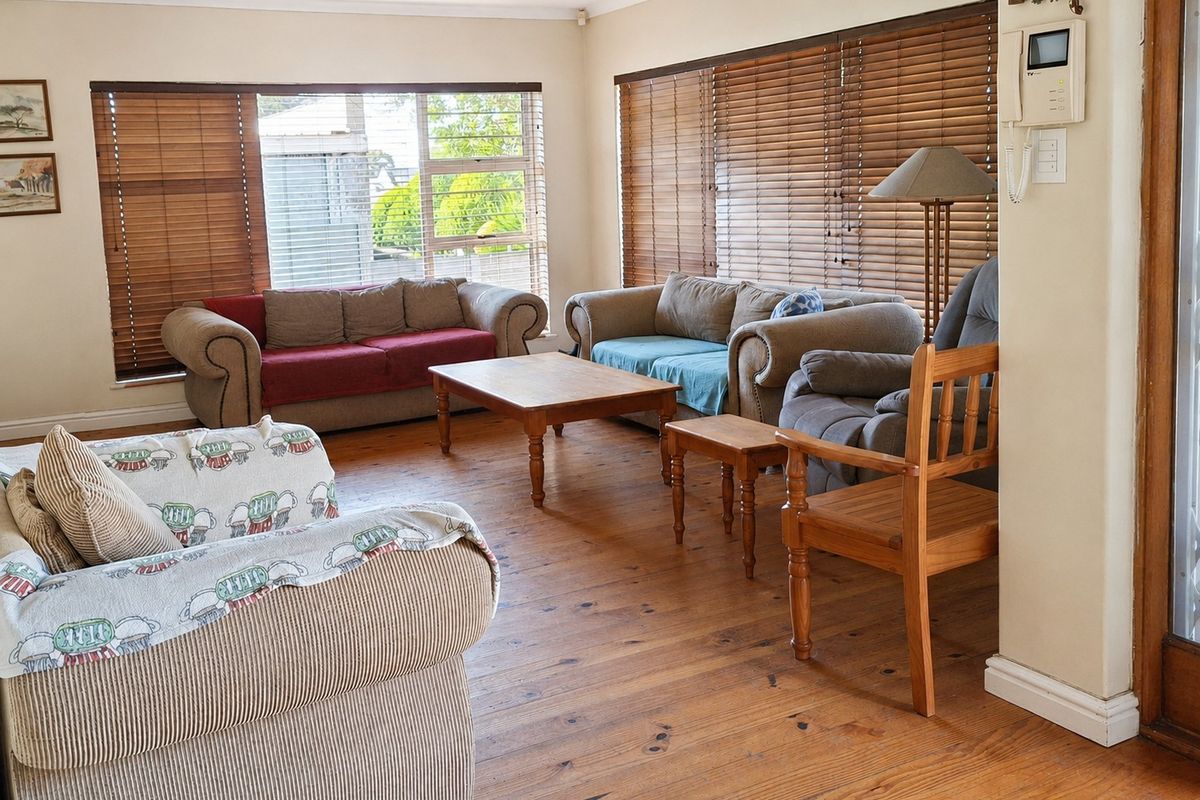 A spacious living room featuring warm timber flooring, large windows with venetian blinds, and recessed downlighting, offering a comfortable and inviting atmosphere.