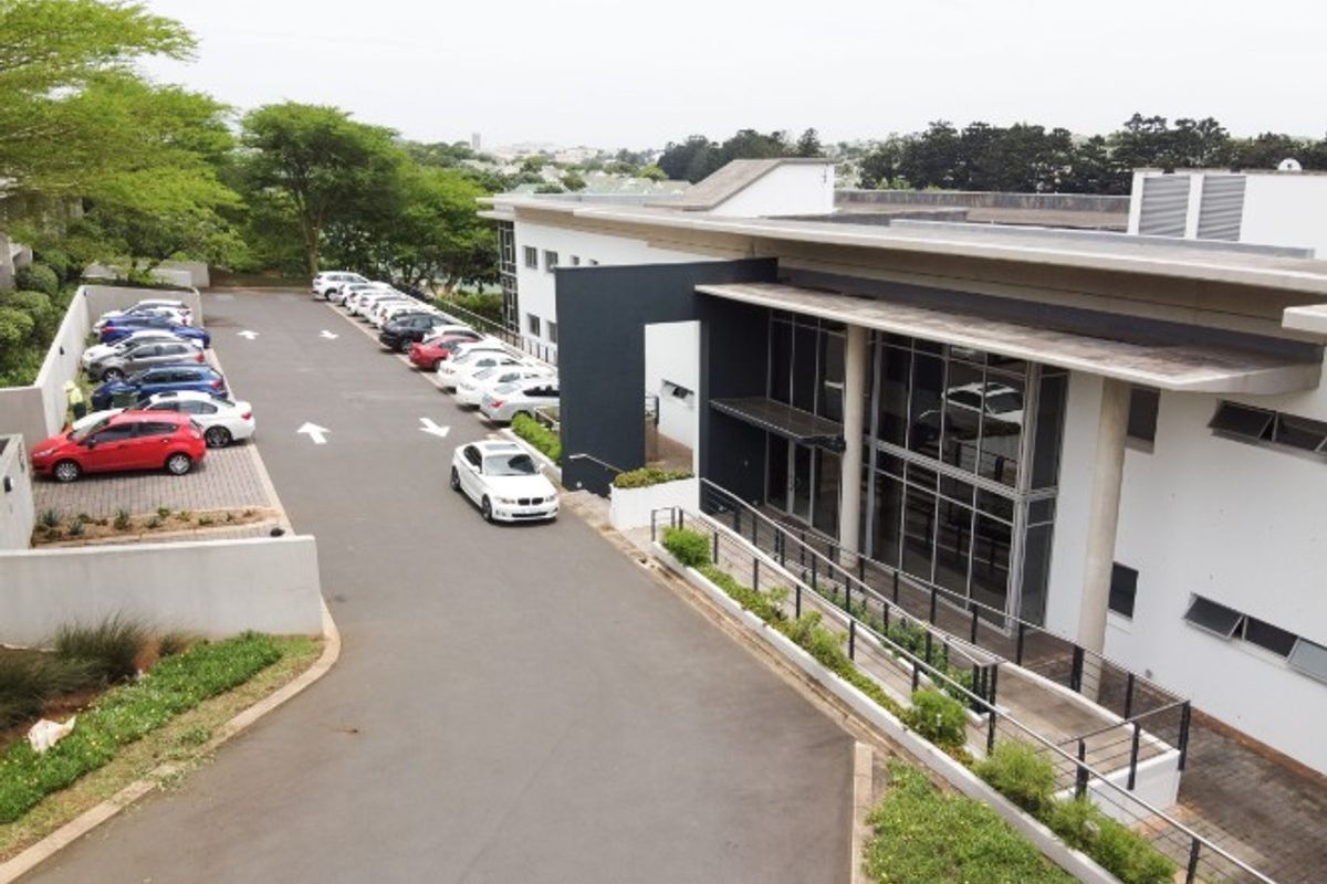 Aerial view of an industrial property featuring a modern building with a glass facade, extensive asphalt parking area, and landscaped retaining walls.
