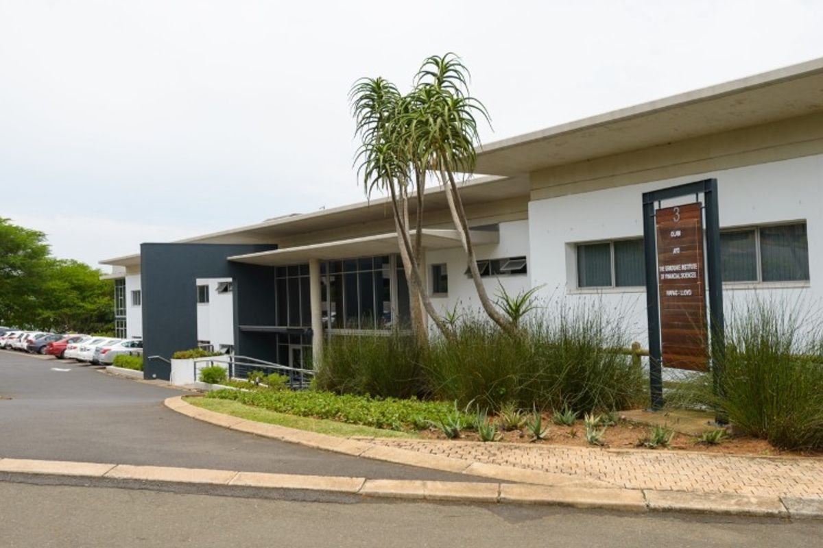 Front exterior view of a modern industrial office building featuring a paved driveway, landscaped garden, and prominent signage.