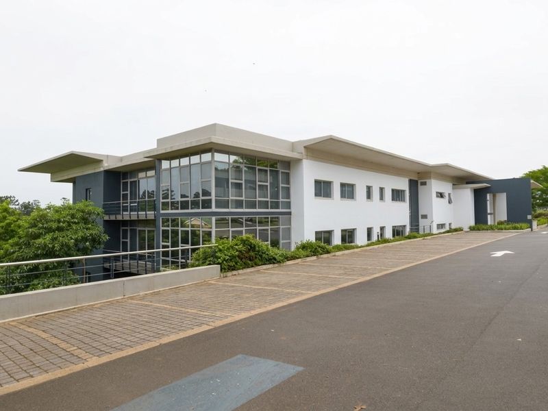 A modern industrial office building featuring extensive glass curtain walling, concrete roof overhangs, and a paved driveway approach.