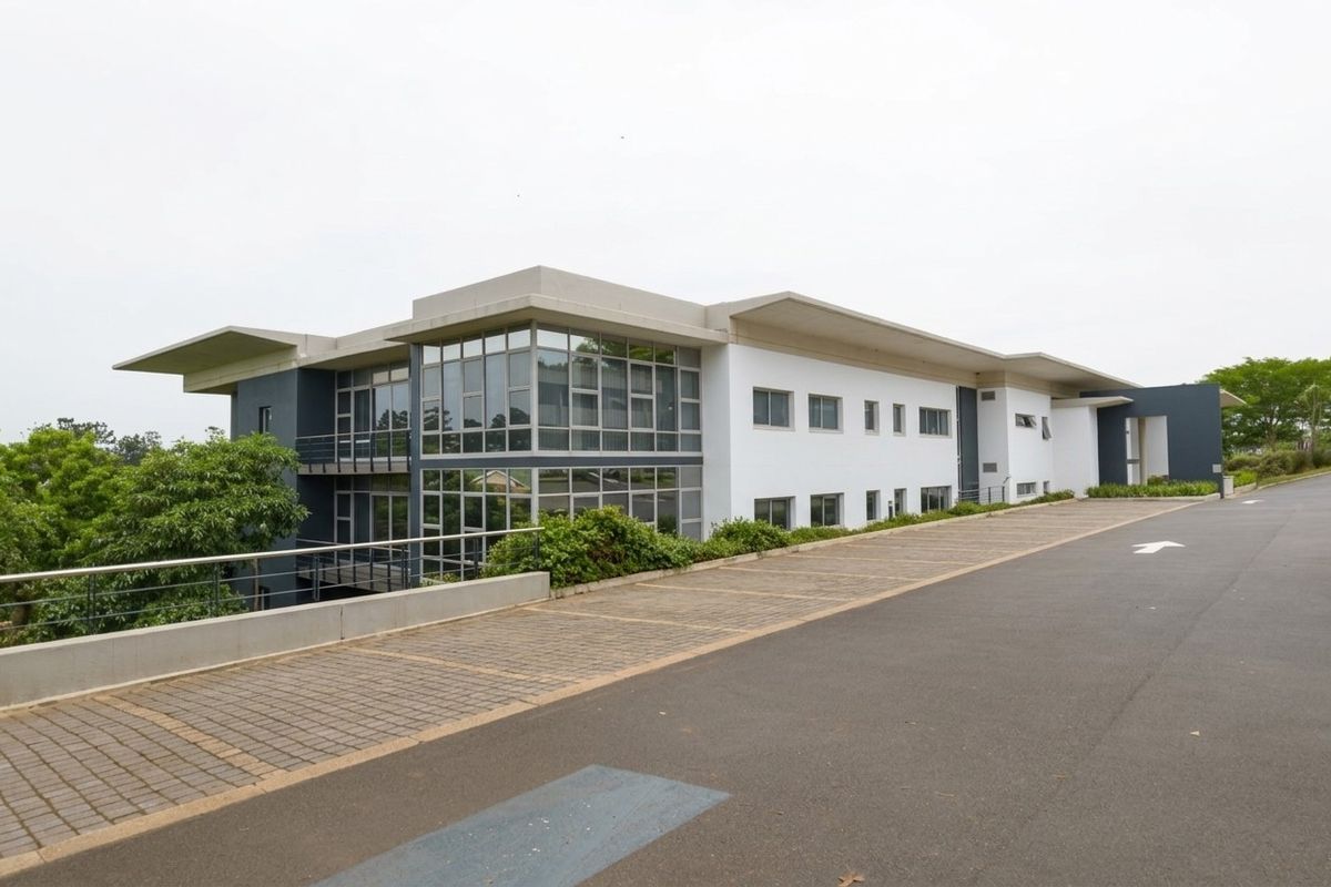 A modern industrial office building featuring extensive glass curtain walling, concrete roof overhangs, and a paved driveway approach.