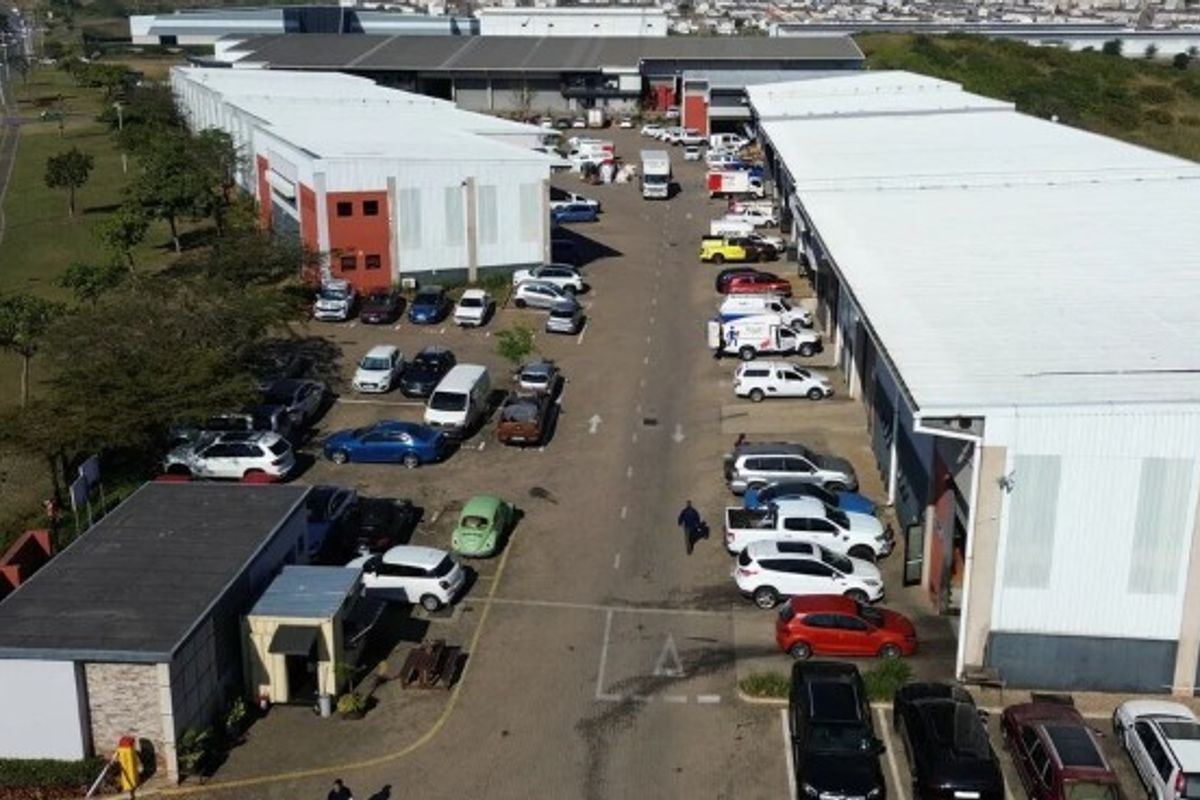 Aerial view of an industrial park featuring multiple warehouse units with metal roofing and a central asphalt driveway for vehicle access.