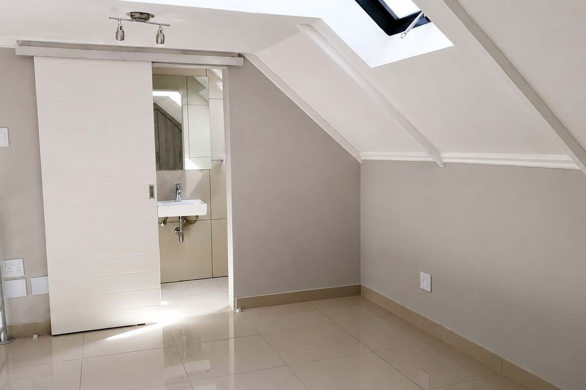 An empty attic-style bedroom featuring a skylight, tiled flooring, and an en-suite bathroom accessed via a sliding door.