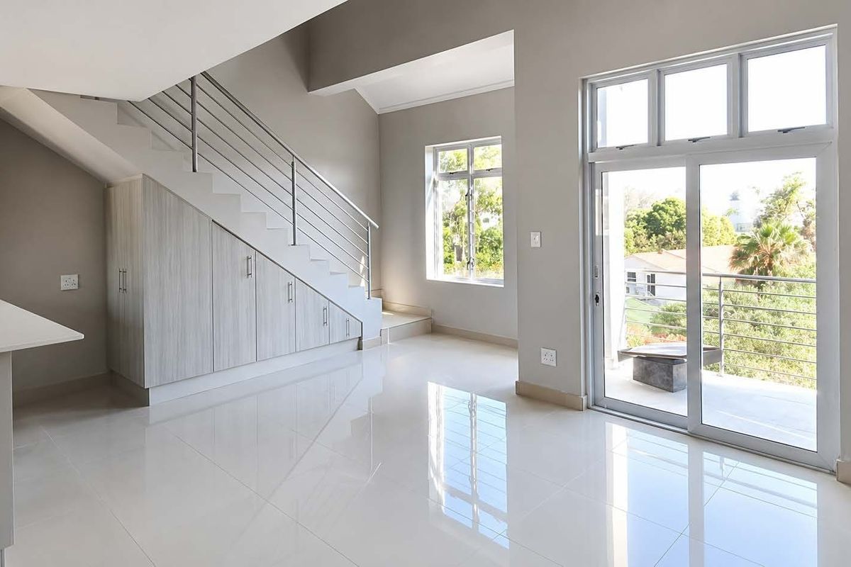 Bright open-plan living area featuring sleek tiled floors, under-stair storage cabinetry, and sliding glass doors leading to a balcony.