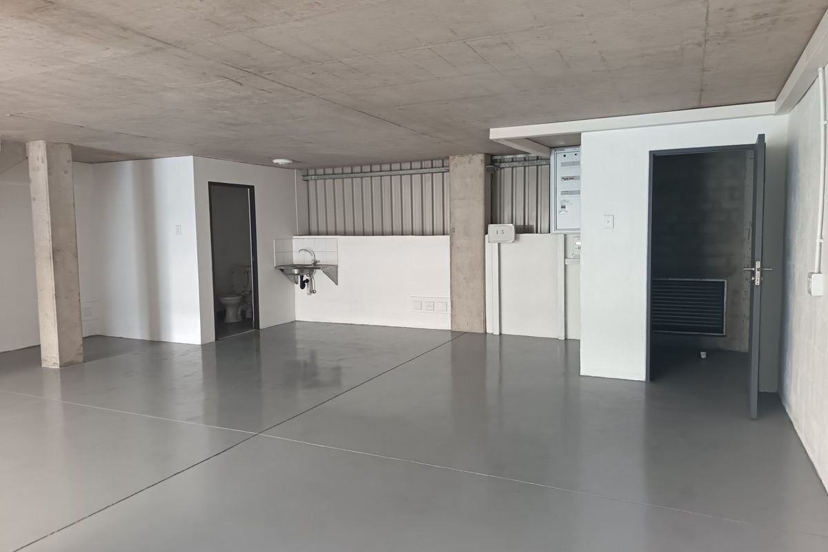 A clean, industrial-style utility space featuring polished epoxy flooring, exposed concrete ceilings, a wall-mounted sink, and an integrated toilet facility.