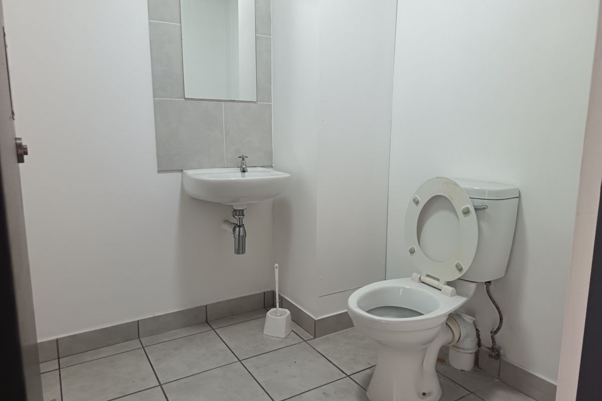 A functional industrial-style bathroom featuring a wall-mounted basin, toilet, and neutral tiled flooring with a tiled splashback.