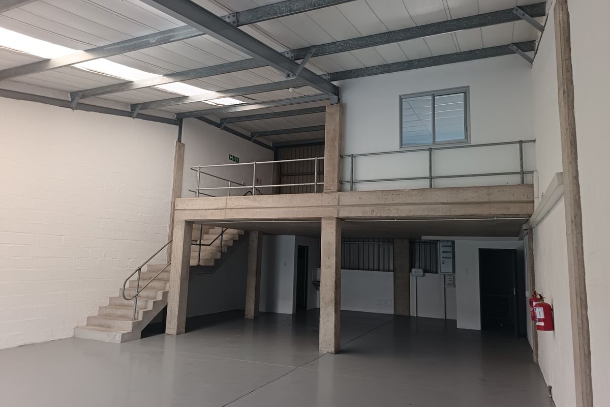Spacious industrial unit featuring a mezzanine level, concrete staircase, exposed steel roof trusses, skylights, and durable epoxy flooring.