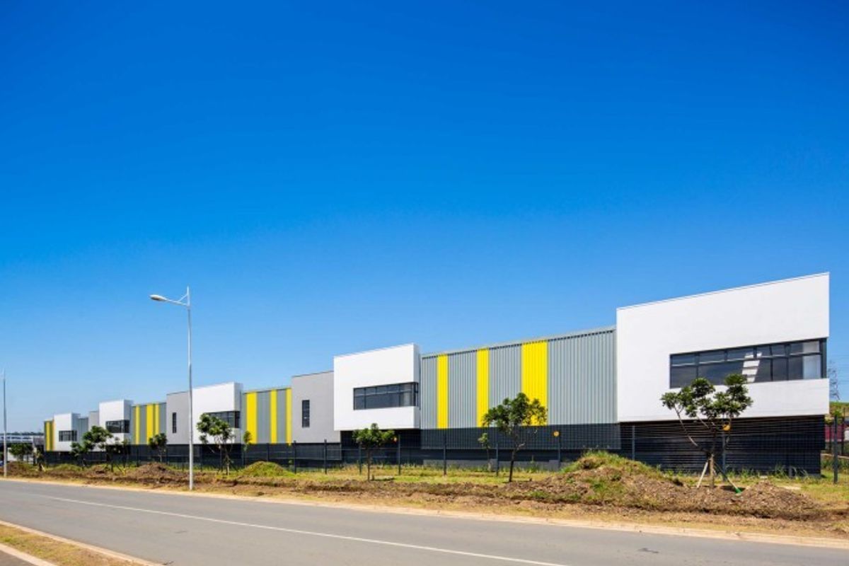 A modern industrial complex featuring a clean, contemporary facade with yellow and grey metal cladding, set back from the road with perimeter fencing.