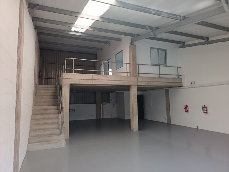 Spacious industrial unit featuring a mezzanine level, concrete flooring, exposed steel roof structure, and natural light provided by overhead skylights.