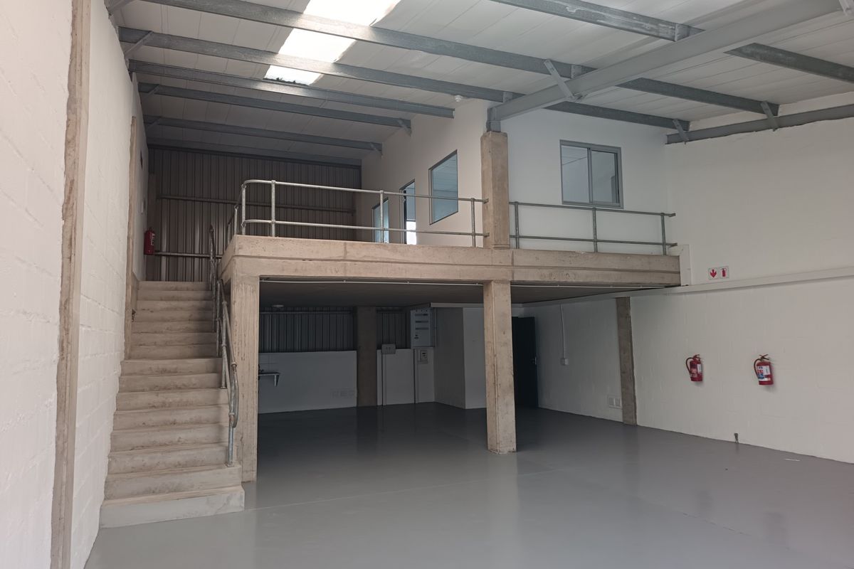 Spacious industrial unit featuring a mezzanine level, concrete flooring, exposed steel roof structure, and natural light provided by overhead skylights.