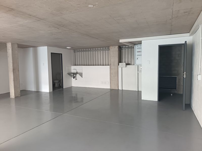 A clean, industrial-style utility space featuring an exposed concrete ceiling, durable epoxy flooring, a wall-mounted sink, and an integrated toilet facility.