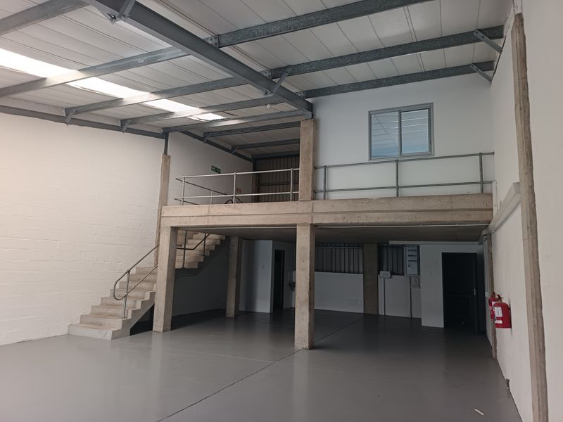 Spacious industrial unit featuring a mezzanine level, concrete staircase with metal railings, exposed steel roof trusses, skylights, and durable epoxy-coated flooring.