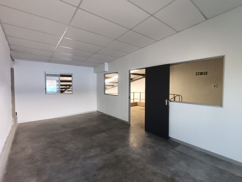 A clean, vacant office space featuring a suspended ceiling, polished concrete flooring, and an internal glass partition with a sliding door.