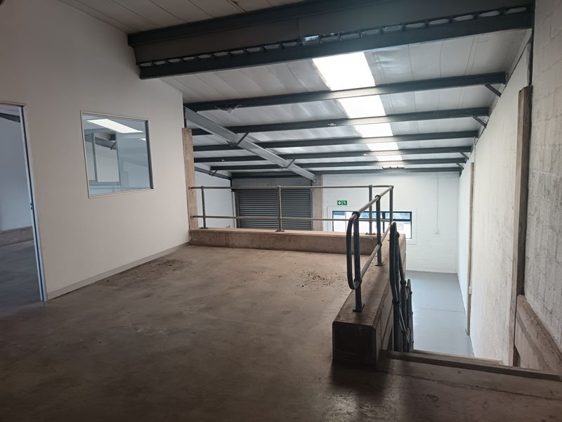 Industrial mezzanine level featuring exposed steel beams, skylights, and metal safety railings, overlooking the main warehouse floor area.