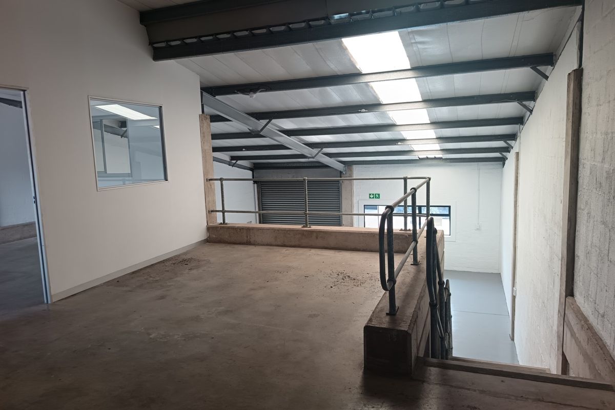 Industrial mezzanine level featuring exposed steel beams, skylights, and metal safety railings, overlooking the main warehouse floor area.