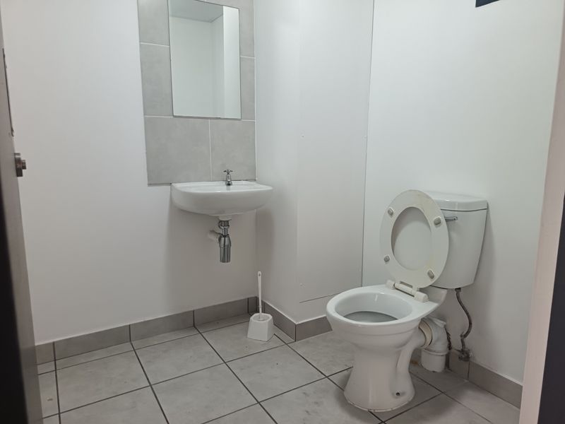 A clean, functional industrial-style bathroom featuring a wall-mounted basin, tiled splashback, and standard toilet with tiled flooring.