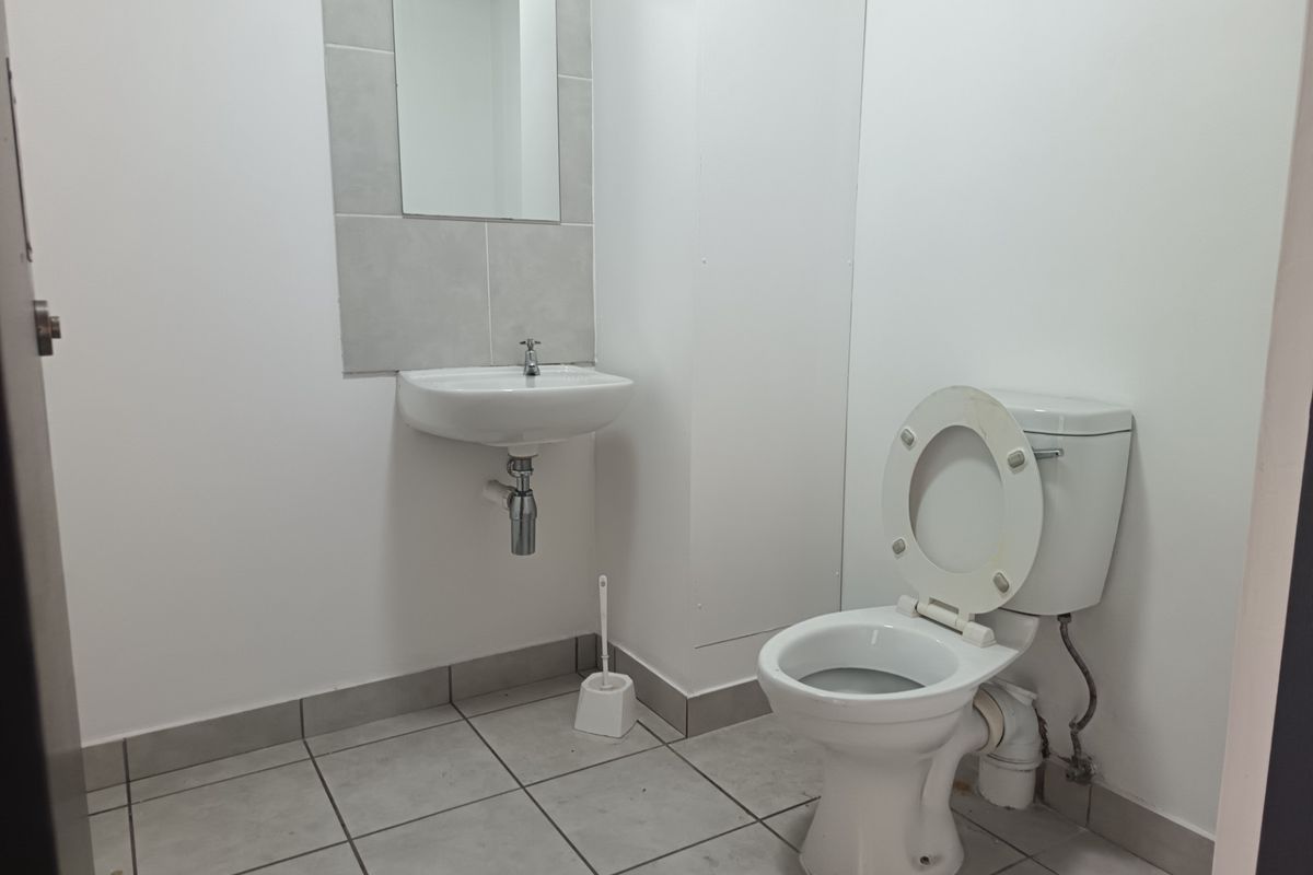 A clean, functional industrial-style bathroom featuring a wall-mounted basin, tiled splashback, and standard toilet with tiled flooring.