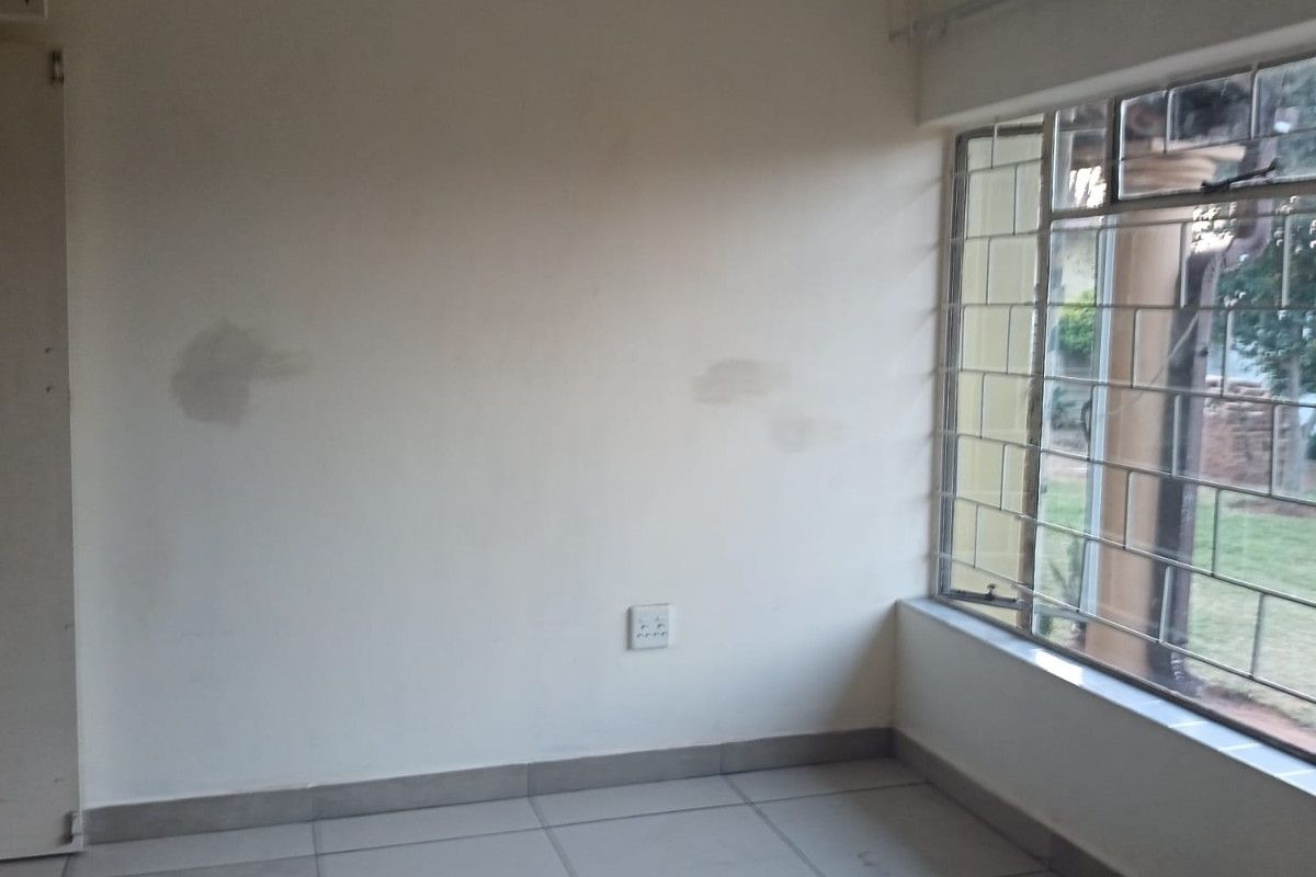 An empty bedroom featuring tiled flooring and security burglar bars on the window, requiring minor cosmetic wall repairs.