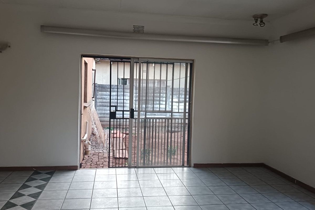 An empty living room featuring tiled flooring and a sliding door with a security gate leading to the exterior.