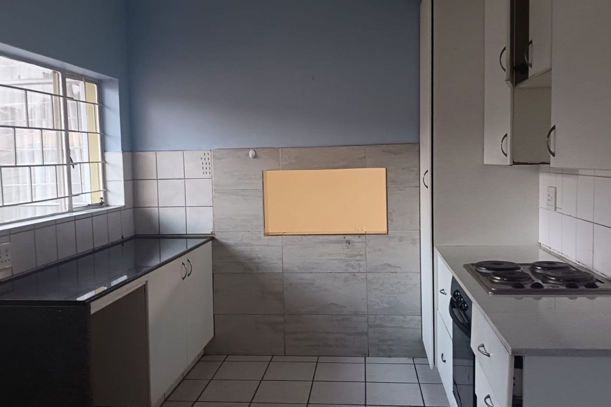 A functional kitchen featuring built-in cabinetry, an electric hob, and an oven, with tiled flooring and splashbacks throughout.