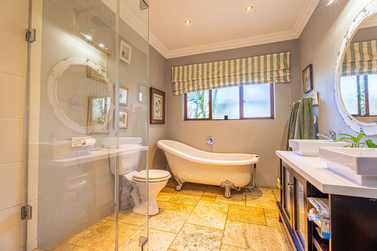 A well-appointed bathroom featuring a classic clawfoot bathtub, a glass-enclosed shower, dual vanity sinks, and elegant stone tile flooring.
