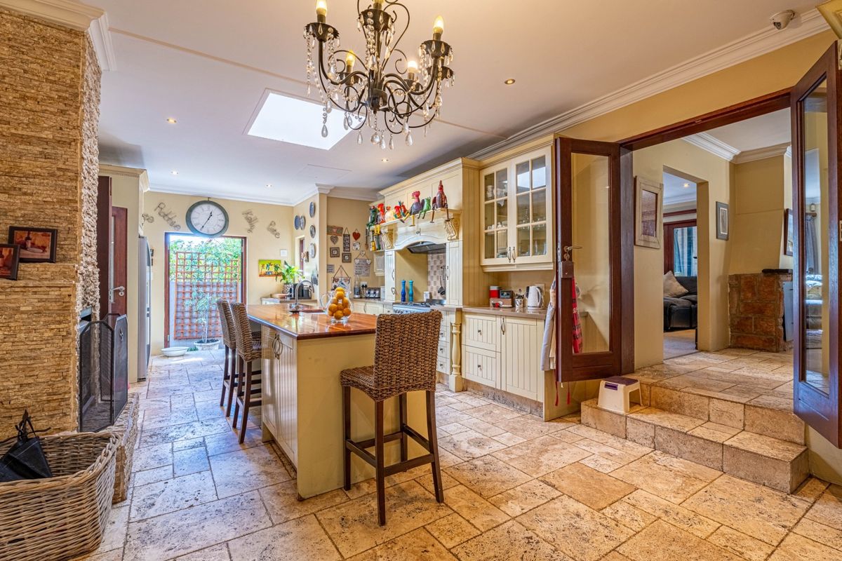 Spacious kitchen featuring a large island with timber countertop, stone-clad fireplace, travertine flooring, and ample built-in cabinetry with glass display units.
