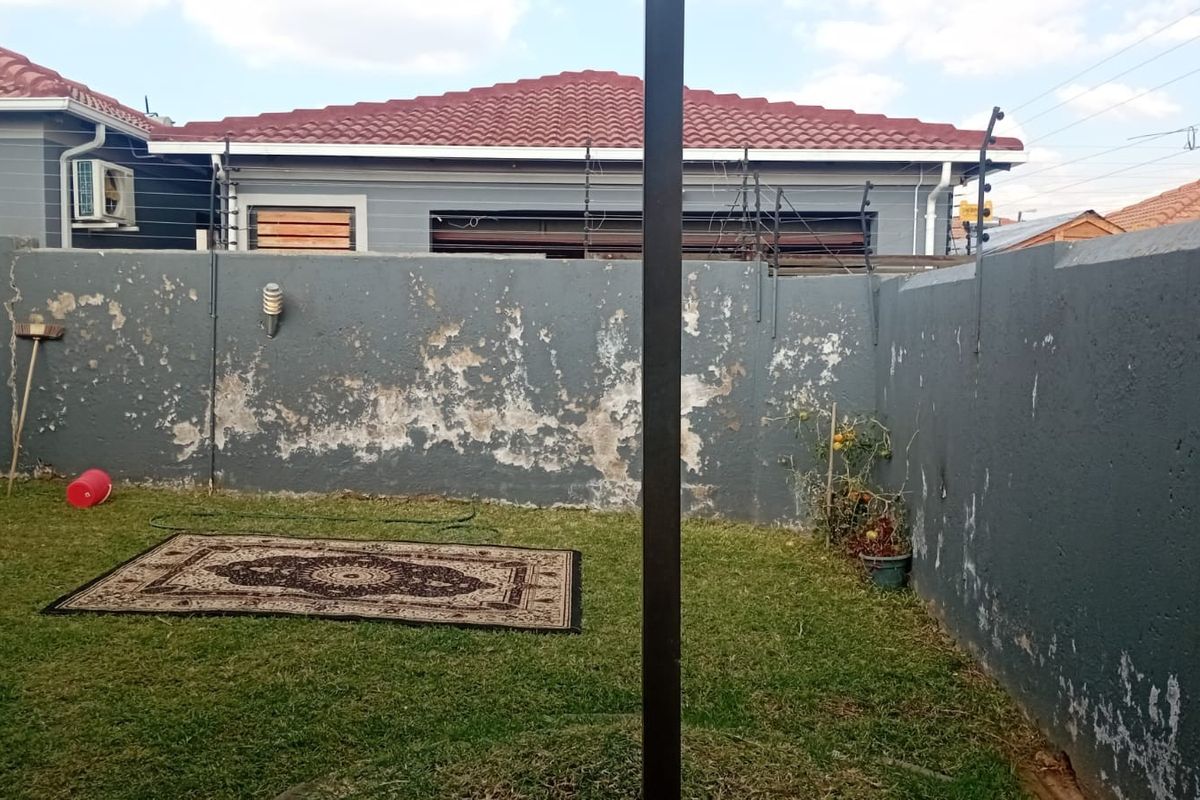 A private rear garden area featuring a lawn and a perimeter wall with electric fencing, currently showing signs of weathered paintwork.