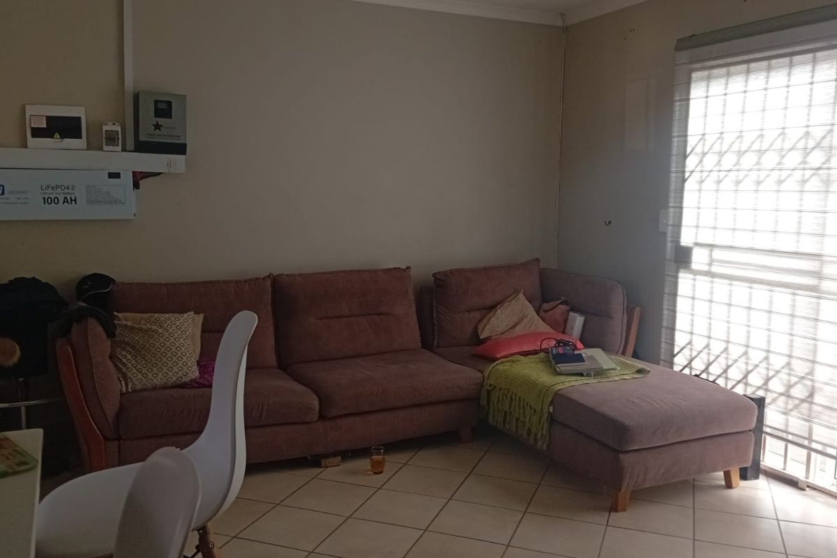 A living room featuring tiled flooring, a sliding door with security gate, and a wall-mounted inverter and battery system.