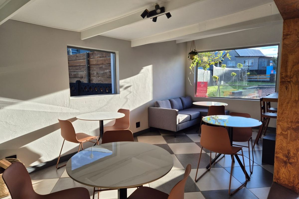 A bright living area featuring tiled flooring, exposed ceiling beams, and large windows providing natural light and garden views.