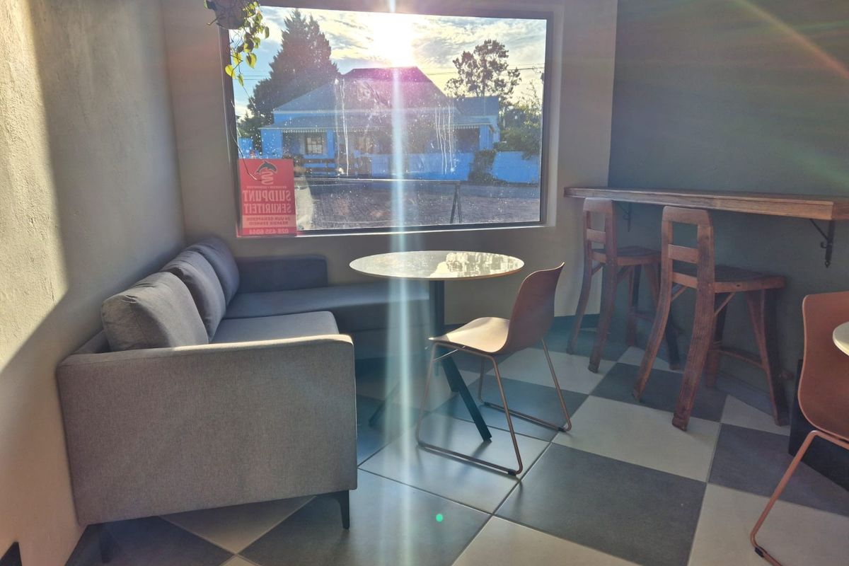 A sunlit living area featuring large windows and checkered floor tiles, offering a bright space with a view of the street.