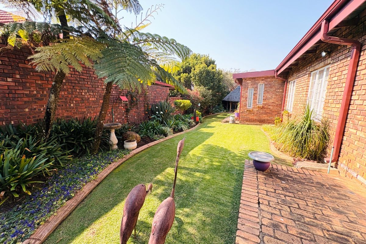 A well-maintained rear garden featuring a brick-paved walkway, lush lawn, and established perimeter face brick walls.