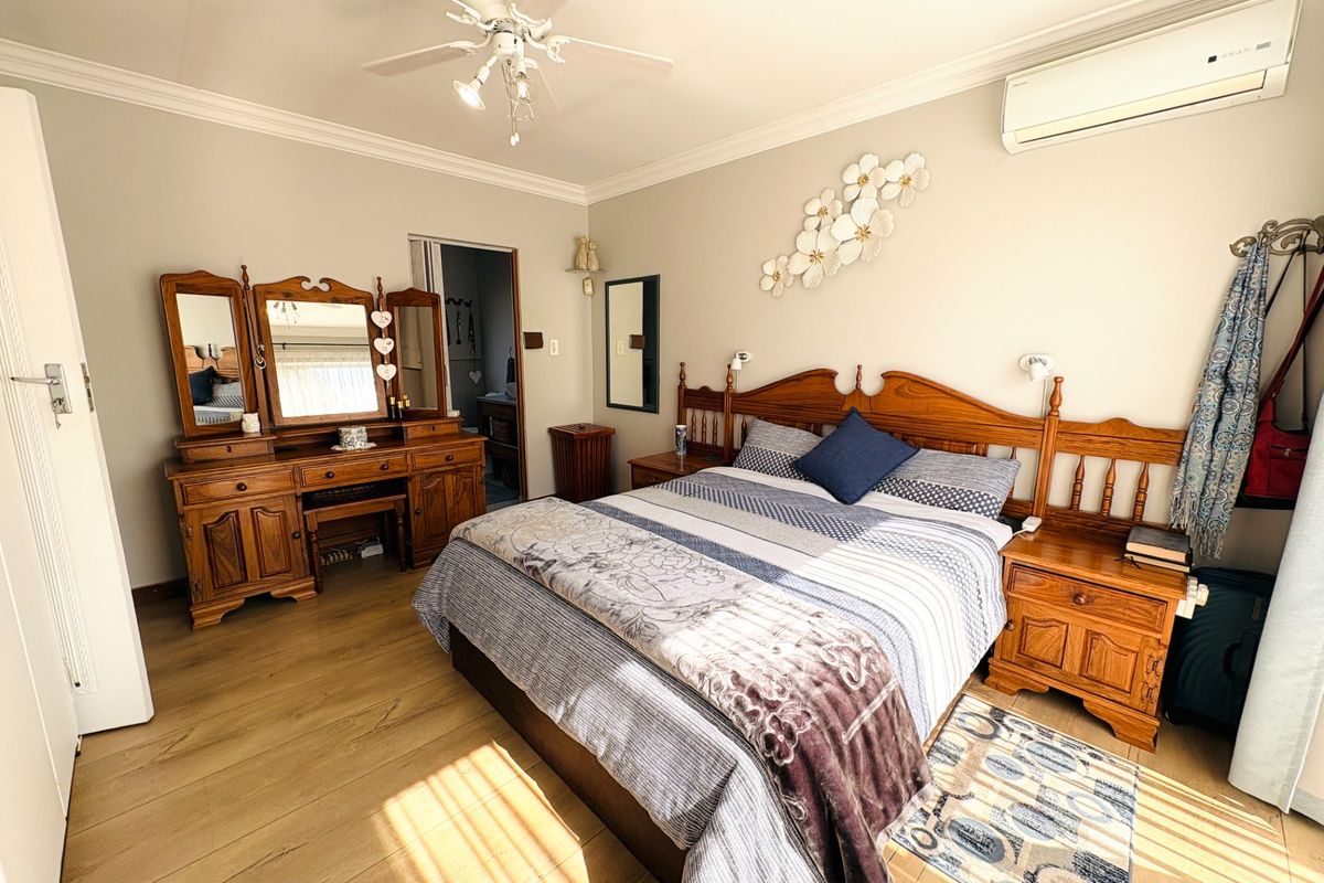 A well-maintained bedroom featuring laminate flooring, crown molding, a ceiling fan, and a wall-mounted split-system air conditioner.