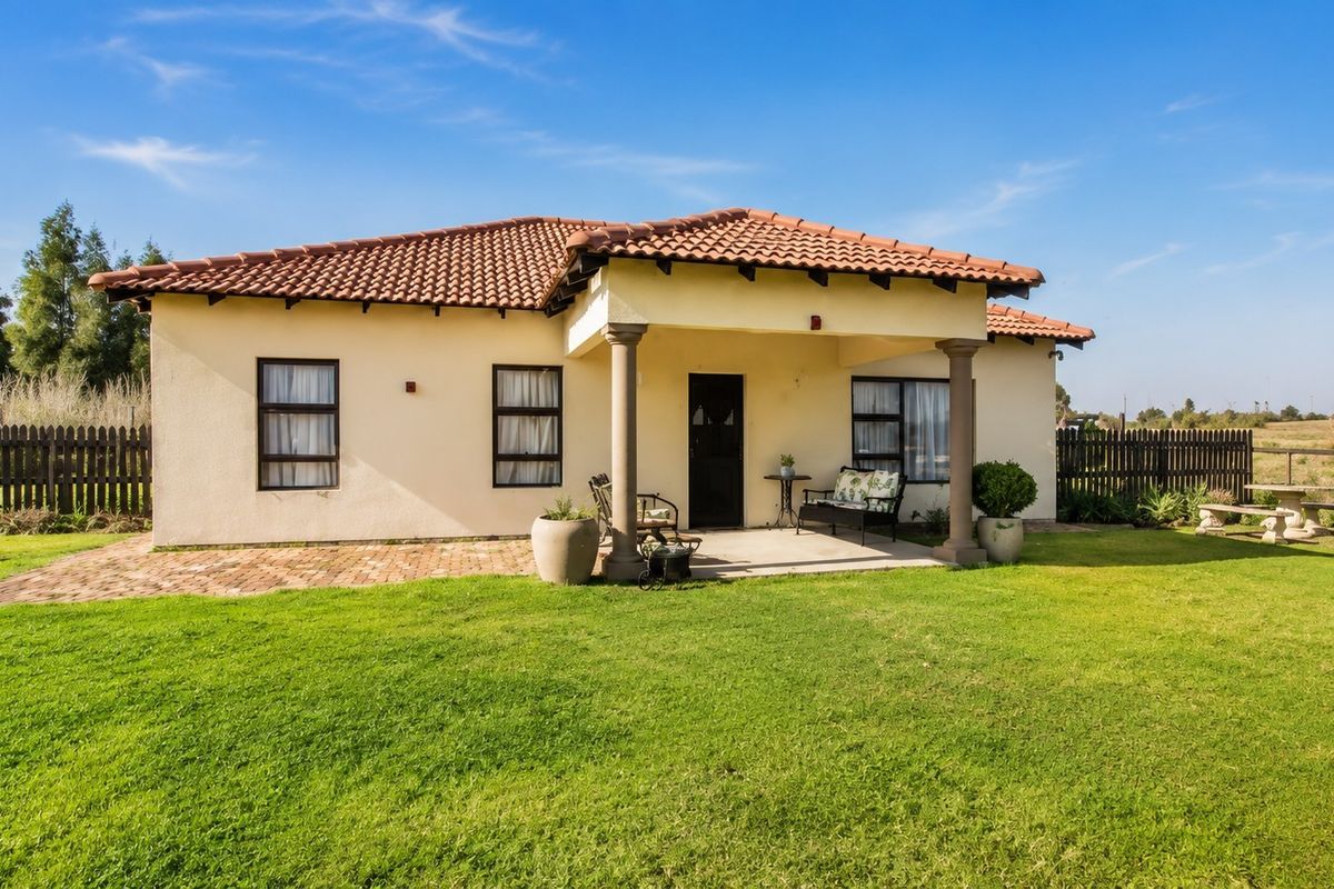 Rear view of a well-maintained small holding residence featuring a covered patio, terracotta tiled roof, and expansive lawn area.