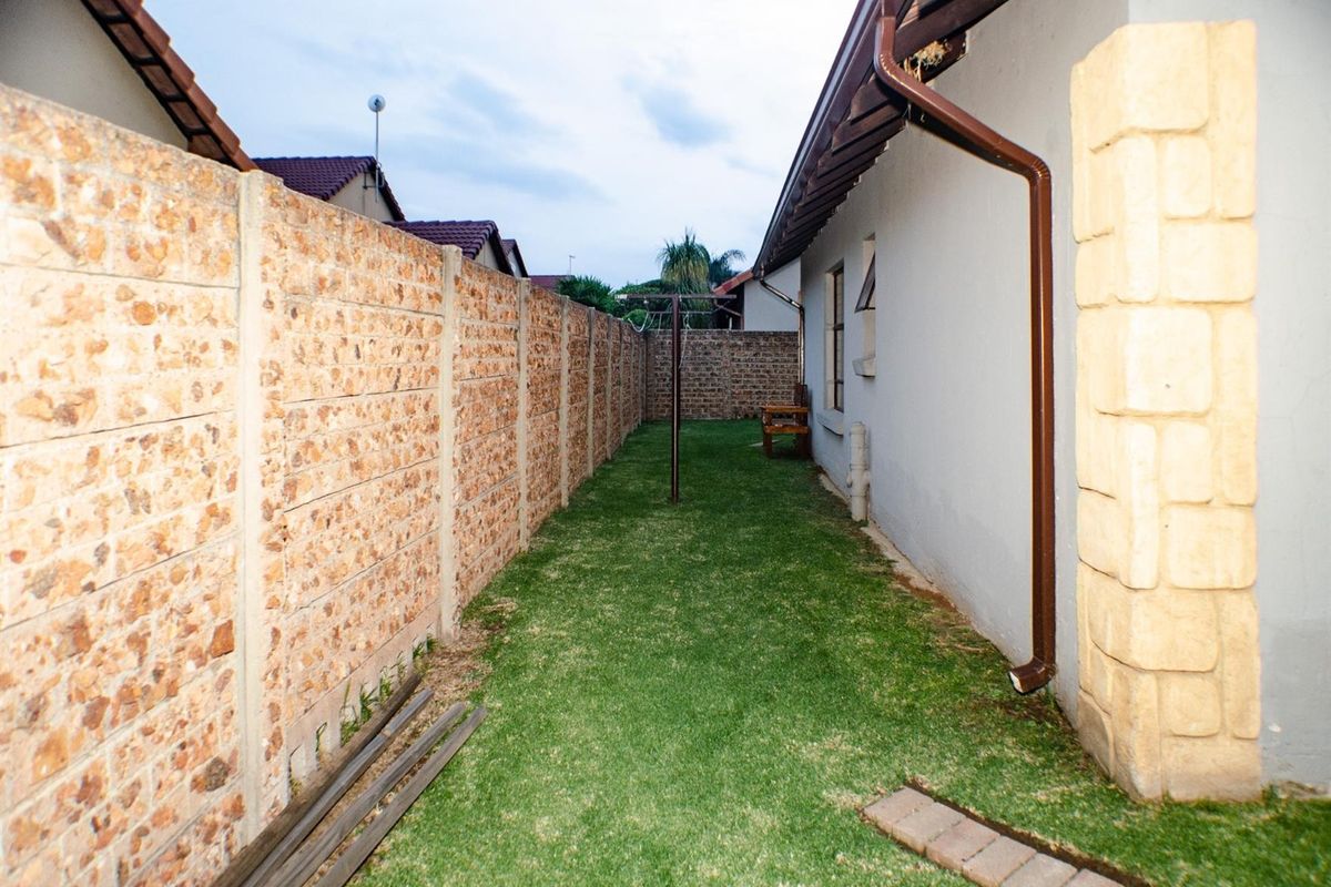 A narrow rear garden area featuring a lawn, enclosed by a combination of precast concrete and brick boundary walls.