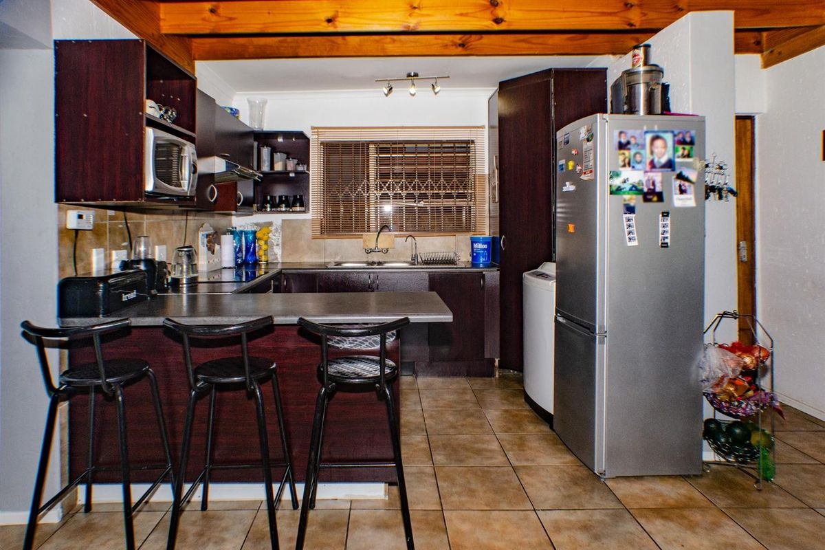 Functional kitchen featuring dark wood cabinetry, laminate countertops, stainless steel sink, and exposed timber ceiling beams with tiled flooring.