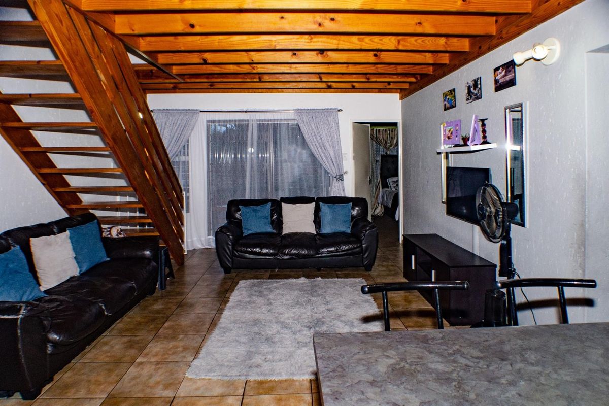 Open-plan living area featuring exposed timber ceiling beams, tiled flooring, and a timber staircase leading to an upper level.
