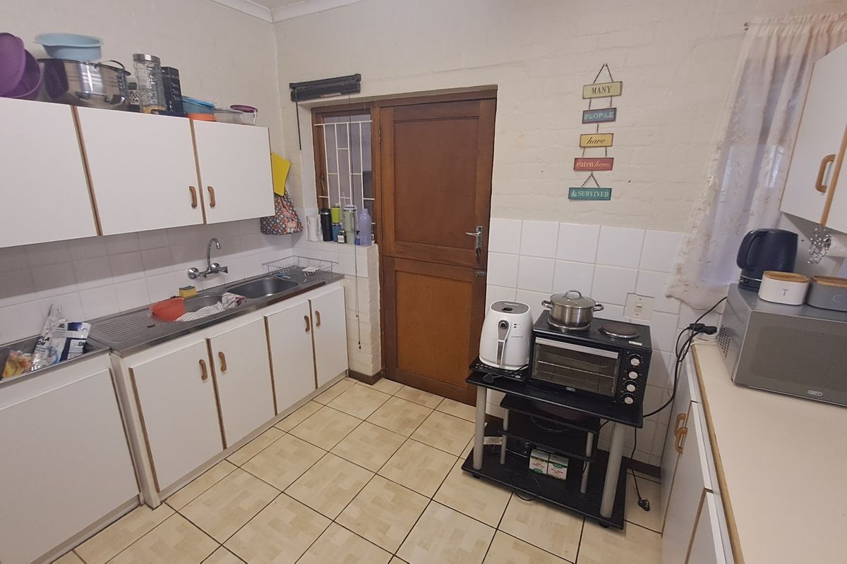 A functional kitchen featuring white cabinetry, tiled splashbacks, and tiled flooring, providing a practical workspace with direct access to an exterior door.