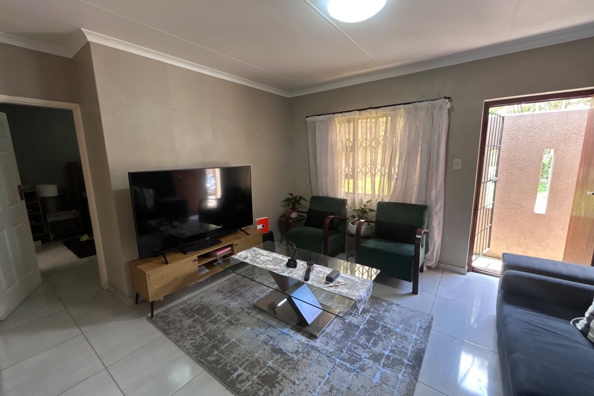 A functional living room featuring tiled flooring, neutral wall tones, and direct access to an outdoor area through a security-fitted door.