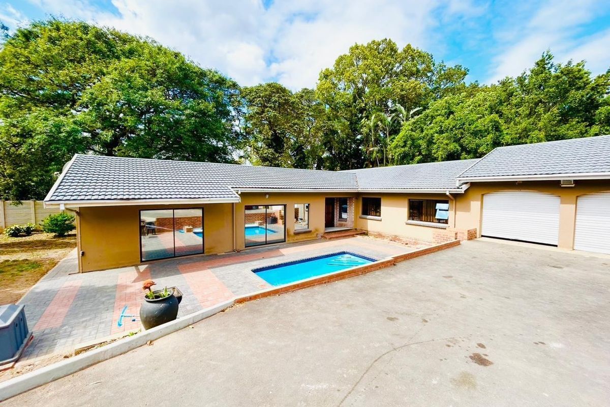 Rear exterior view of a cottage featuring a swimming pool, paved patio area, and attached garage with a concrete driveway.