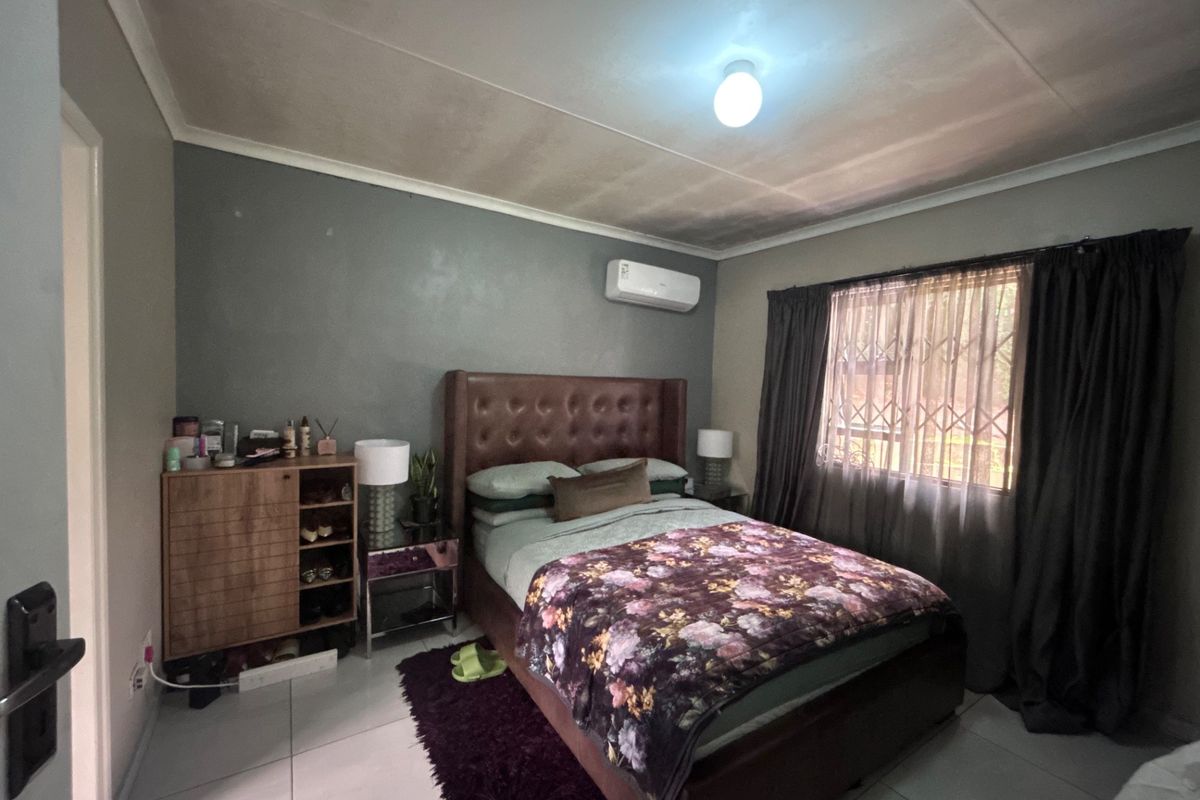 A bedroom featuring tiled flooring, an air conditioning unit, and a window fitted with a security gate.