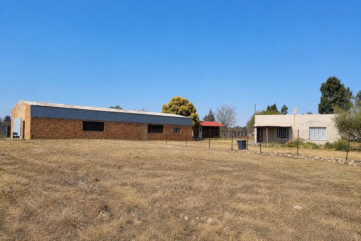 View of the property grounds featuring a large brick outbuilding and the main residential dwelling set within a rural small holding landscape.
