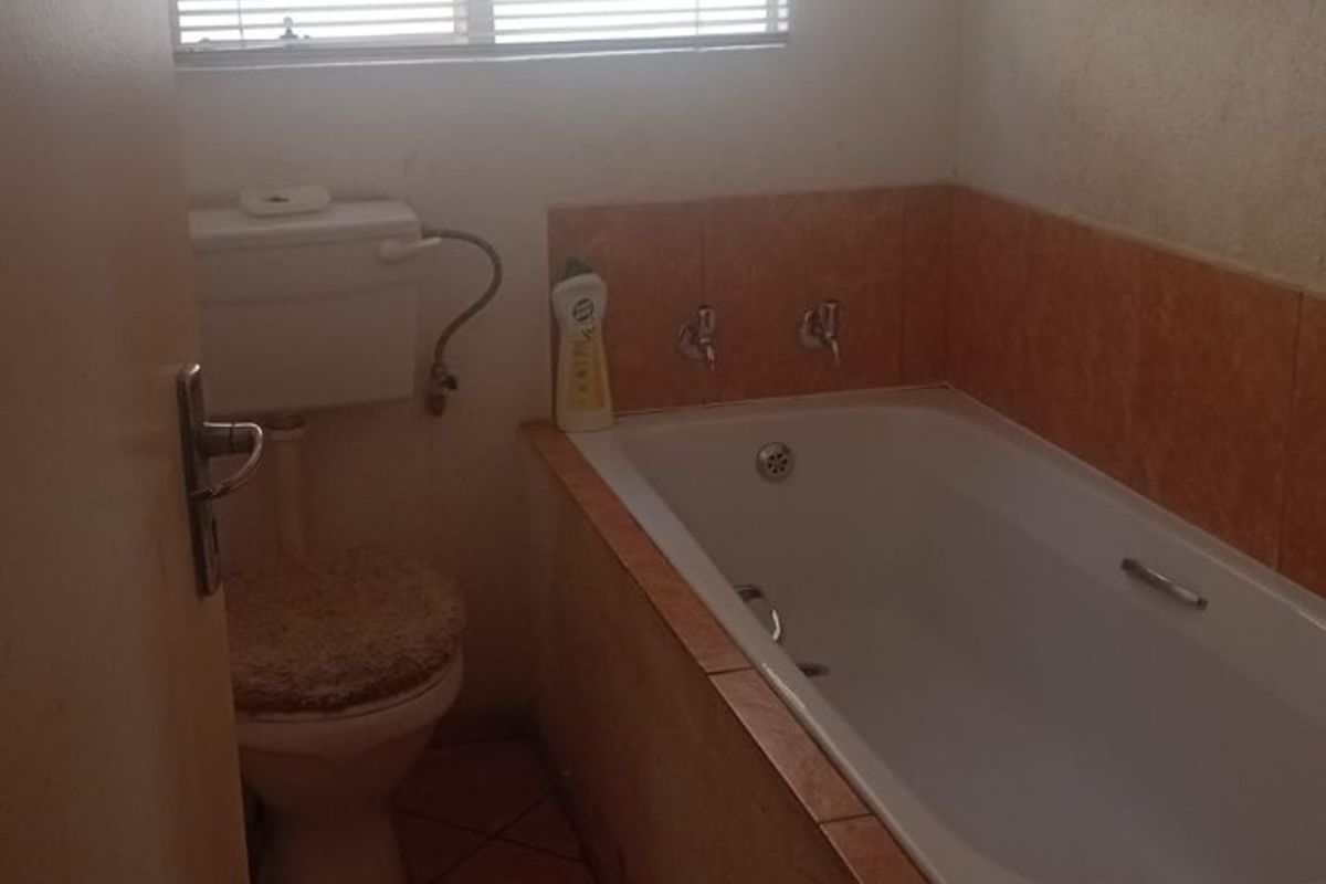 A dated bathroom featuring a built-in bathtub, ceramic tiling, and a standard toilet, requiring cosmetic updates to improve its overall appeal.