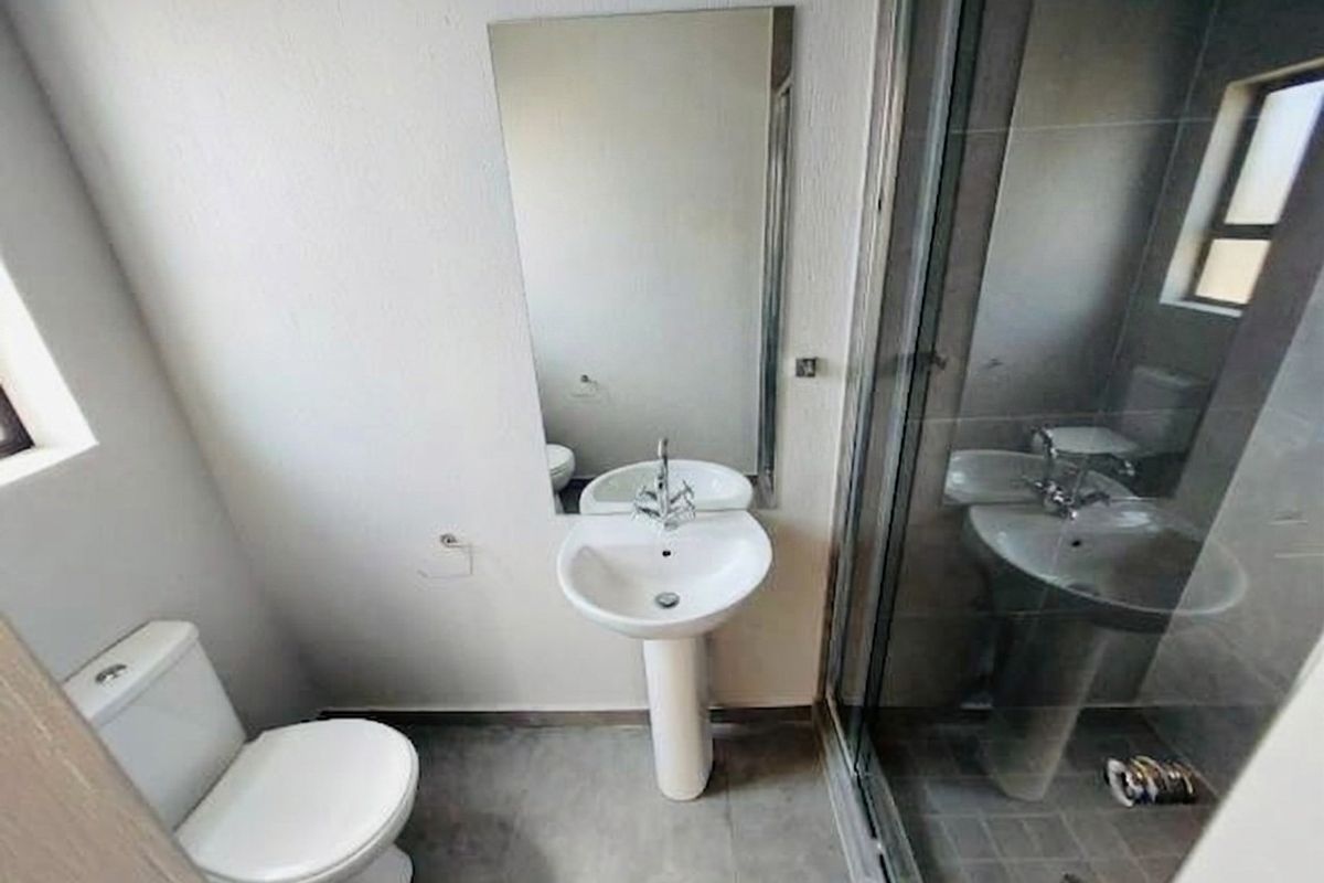 A functional bathroom featuring a pedestal basin, toilet, and a glass-enclosed shower with tiled flooring and a wall-mounted mirror.