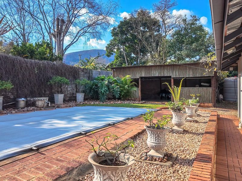 Outdoor pool area featuring a covered swimming pool, brick paved surround, and a detached outbuilding set within a landscaped garden.