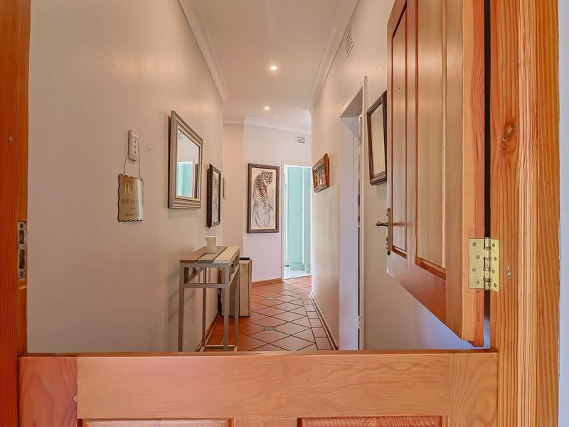 A bright hallway featuring terracotta floor tiles, recessed downlighting, and a solid timber door frame leading into the home.